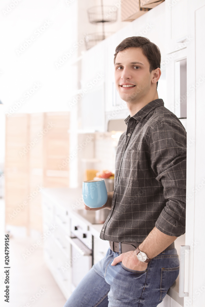 Portrait of confident young man with cup in kitchen