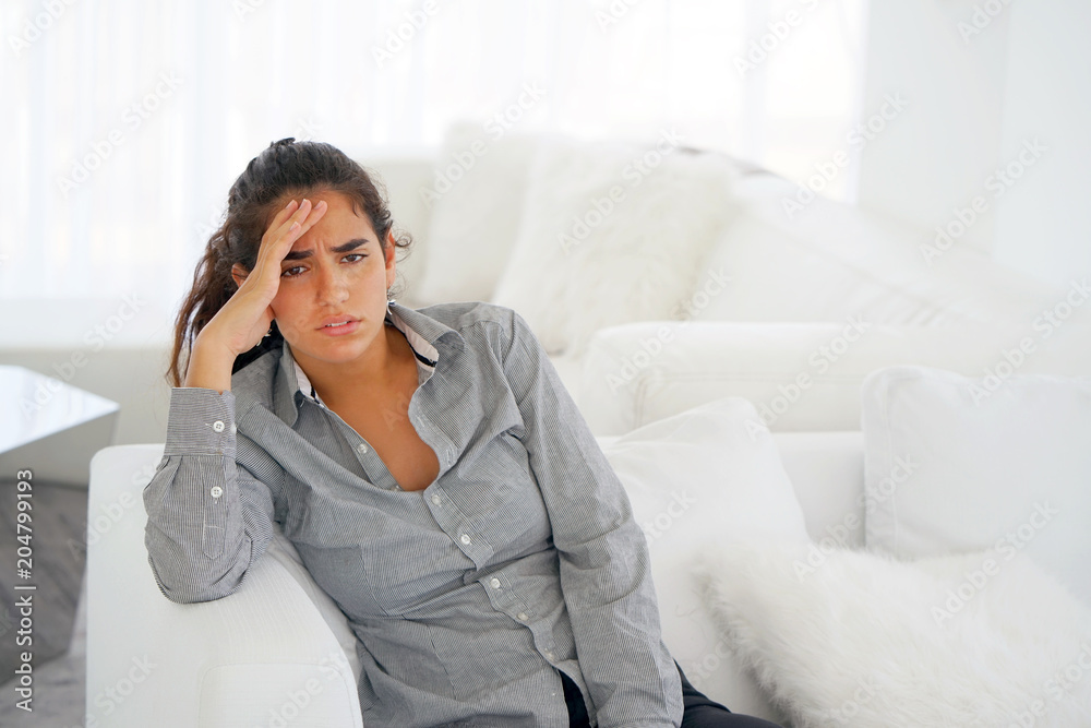 Young woman suffering from headache migraine pain at home on sofa. Health problem, stress and depression. Female holds head with hand. Concept of health. Young woman suffering from headache migraine pain at home on sofa. Health problem, stress and depression. Female holds head with hand. Concept of health.