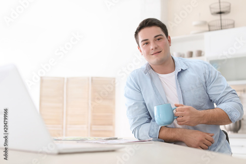 Portrait of confident young man with laptop and cup at table