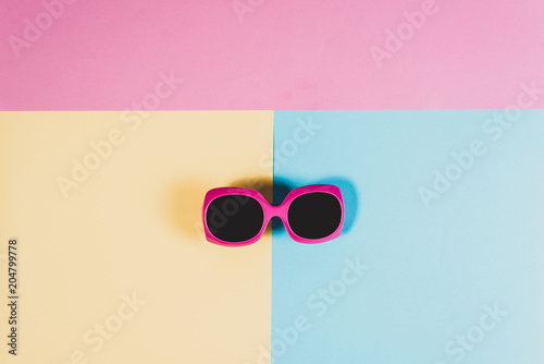 Studio shot of pink sunglasses. Summer is coming concept. Minimal style, minimalist photography. Top view of spread sunglasses on colorful paper backdrop. Pink, yellow and blue pastel colors.