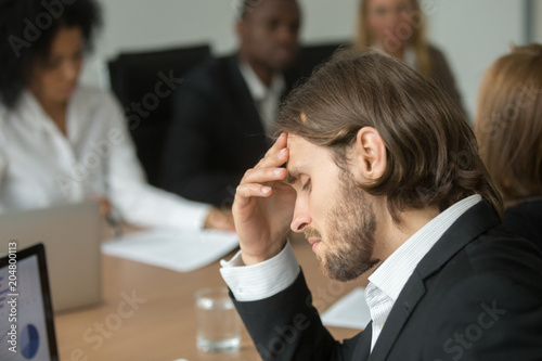 Obraz na plátně Frustrated tired businessman having headache at team meeting, upset company ceo