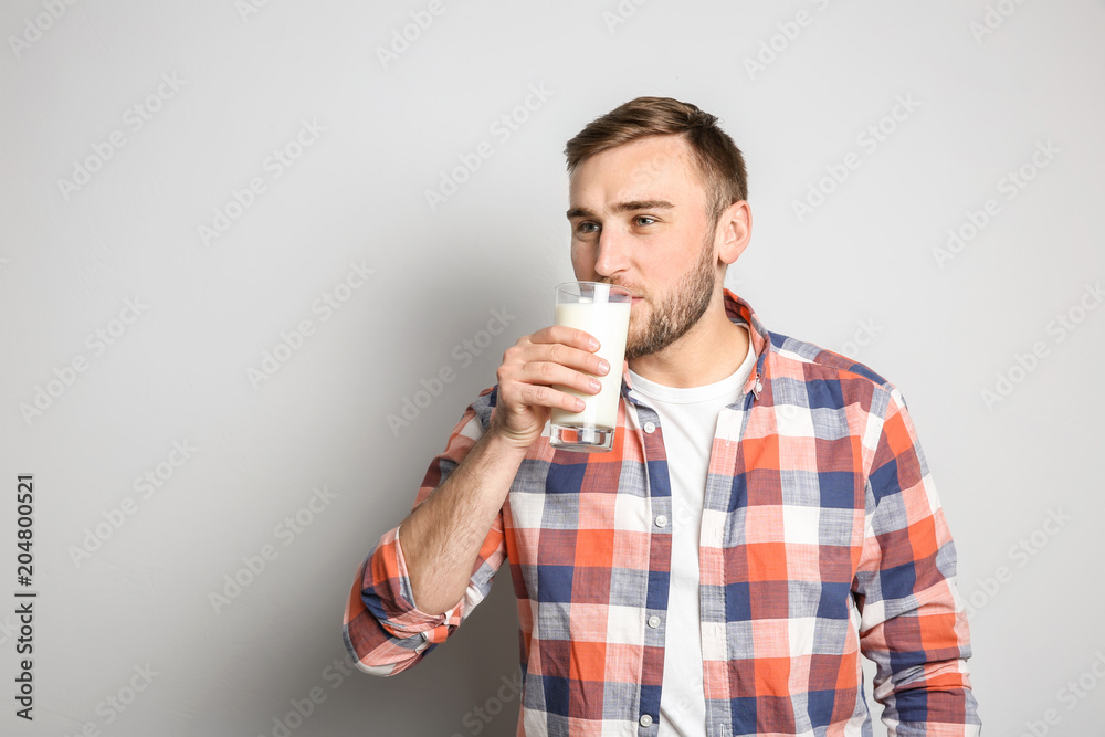Young man drinking tasty milk on light background Young man drinking tasty milk on light background
