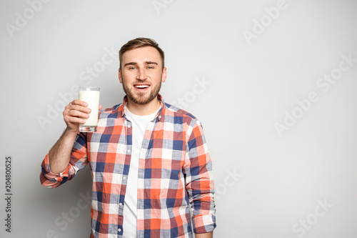 Young man with glass of tasty milk on light background
