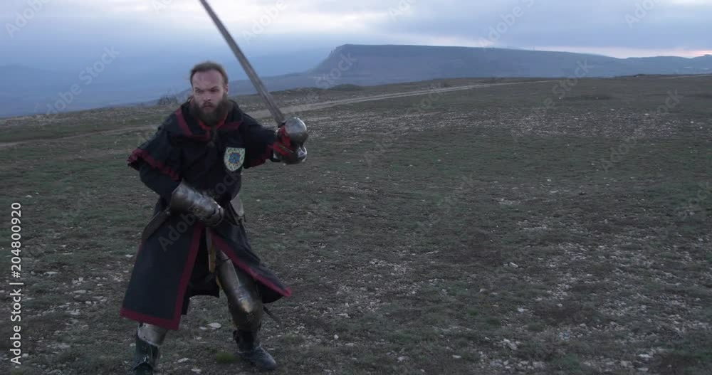 Knight fencing his sword against the backdrop of the mountains at sunset Knight fencing his sword against the backdrop of the mountains at sunset