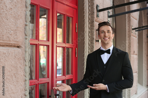 Young doorman in elegant suit standing near restaurant entrance