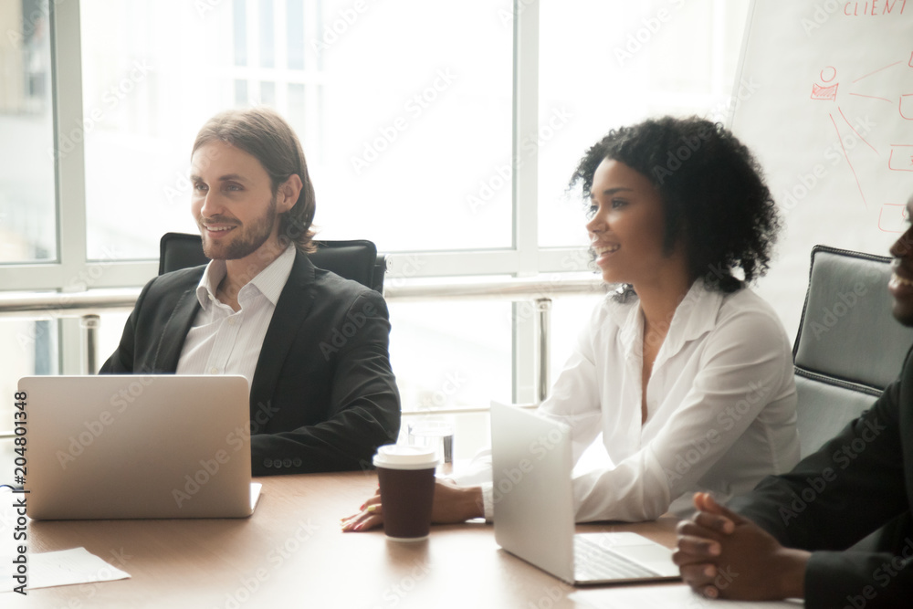 Obraz premium Multiracial smiling business people participating group meeting sitting at conference table, interested diverse happy partners board team members attentively listening to new ideas at briefing