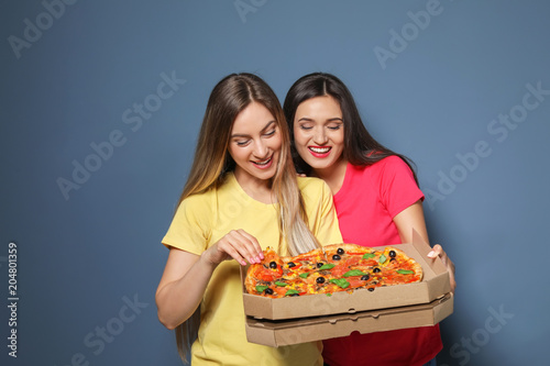 Attractive young women with delicious pizza on color background