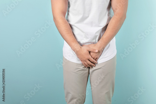 Young man with urological problems suffering from pain on color background