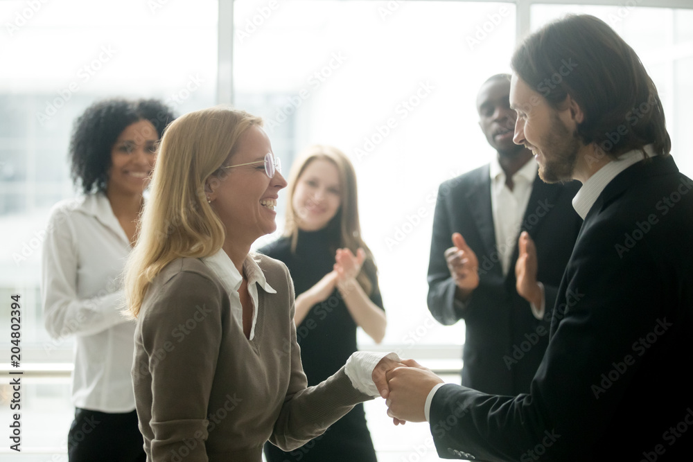 Boss handshaking rewarding motivating successful female employee congratulating with promotion, appreciating good work results, making partnership deal, expressing respect while colleagues applauding Boss handshaking rewarding motivating successful female employee congratulating with promotion, appreciating good work results, making partnership deal, expressing respect while colleagues applauding