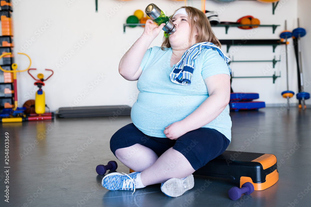 Full length portrait of exhausted obese woman sitting on step and
