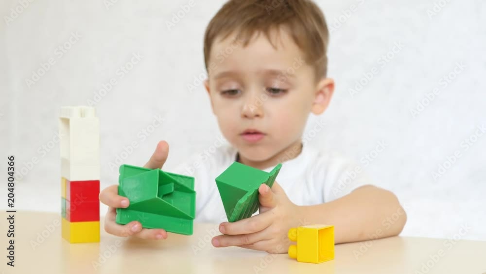 A child is playing in colored blocks, sitting at a table on a white background. Child and toys. Focus camera is aimed at toys. A child is playing in colored blocks, sitting at a table on a white background. Child and toys. Focus camera is aimed at toys.