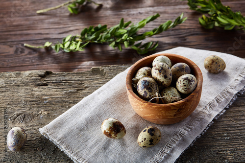 Rural still life with bowl full of eggs quail, eggs on a homespun napkin, boxwood on wooden background, top view photo