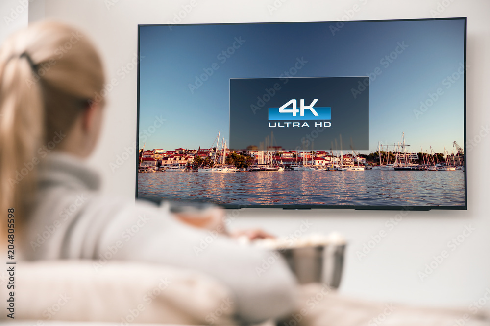 Big modern TV with 4k resolutions and young woman on foreground watching some video - obrazy, fototapety, plakaty 