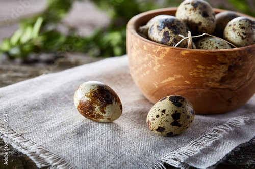 Rural still life with bowl full of eggs quail, eggs on a homespun napkin, boxwood on wooden background, top view photo