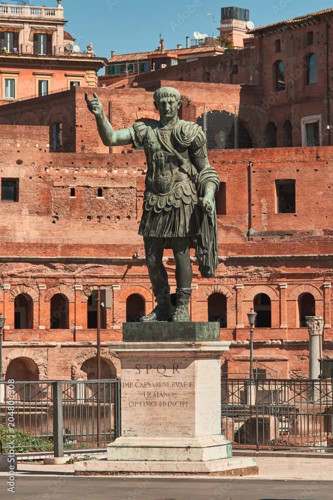 Obraz premium Rome, Bronze statue of emperor Caesar Nervae Trajan, Forum of Caesar Nervae Trajan in the background