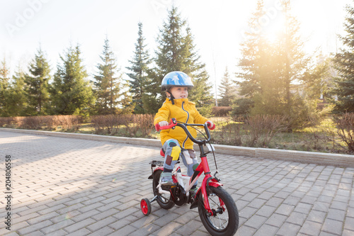 3 years old happy toddler boy riding red bike. Little kid learns to ride a bicycle. Sport, cycling, active playing, and childhood concept. First four-wheeled bike for little child. © uv_group