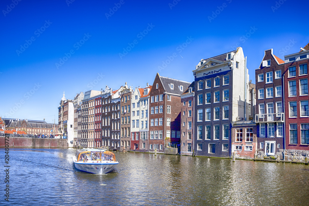 People at Tourist Boat Attraction in Amsterdam at Damrak Canal With Boat Going to Pier in the Netherlands