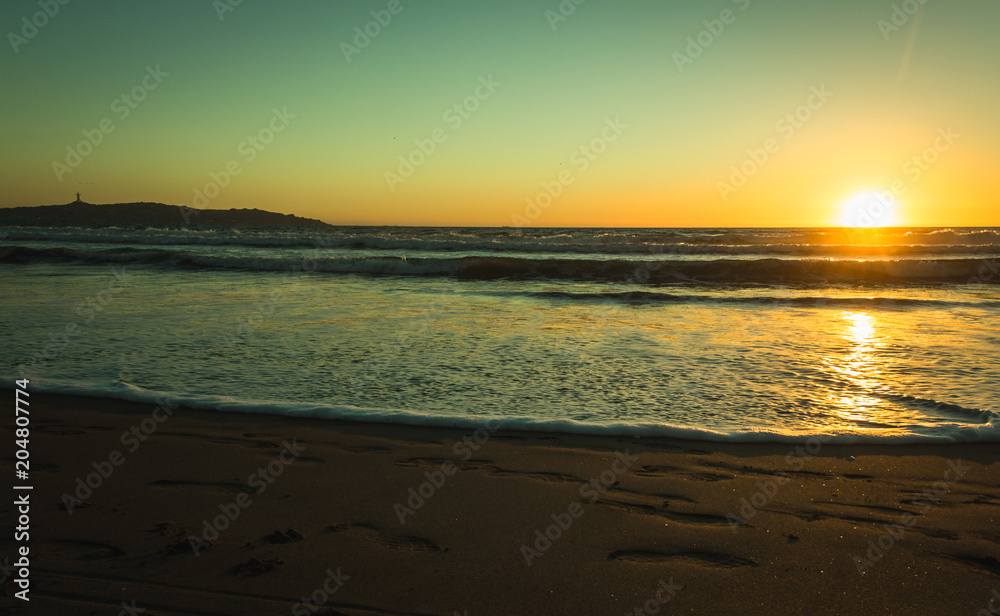 Splendid sunset with footprints on sand and city of Coquimbo on the background in La Serena beach, Chile