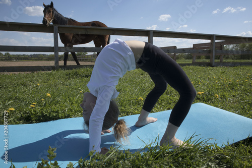 The young girl is engaged in gymnastics on the grass healthy lifestyle. Child girl doing gymnastics. Little cute girl practicing yoga pose on the background of the paddock with a horse photo