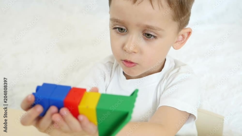 Child boy playing with colored blocks, in slow motion. The camera moves from the child's face to the toys, in slow motion Child boy playing with colored blocks, in slow motion. The camera moves from the child's face to the toys, in slow motion