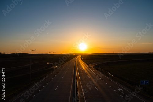 Paved four-lane highway stretches to the sunset. Clear cloudless sky. © Yuliya Bodziak
