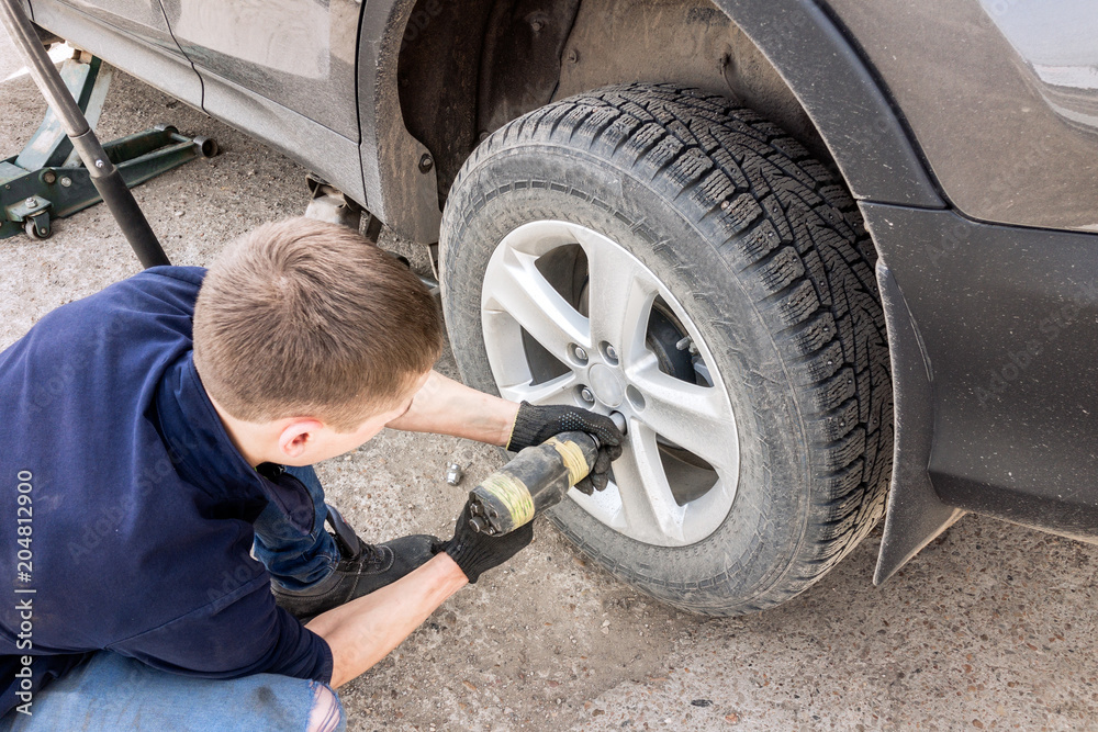 Man working in repair service and fixing wheel to car using screwdriver. Man screwing wheel to car Man working in repair service and fixing wheel to car using screwdriver. Man screwing wheel to car