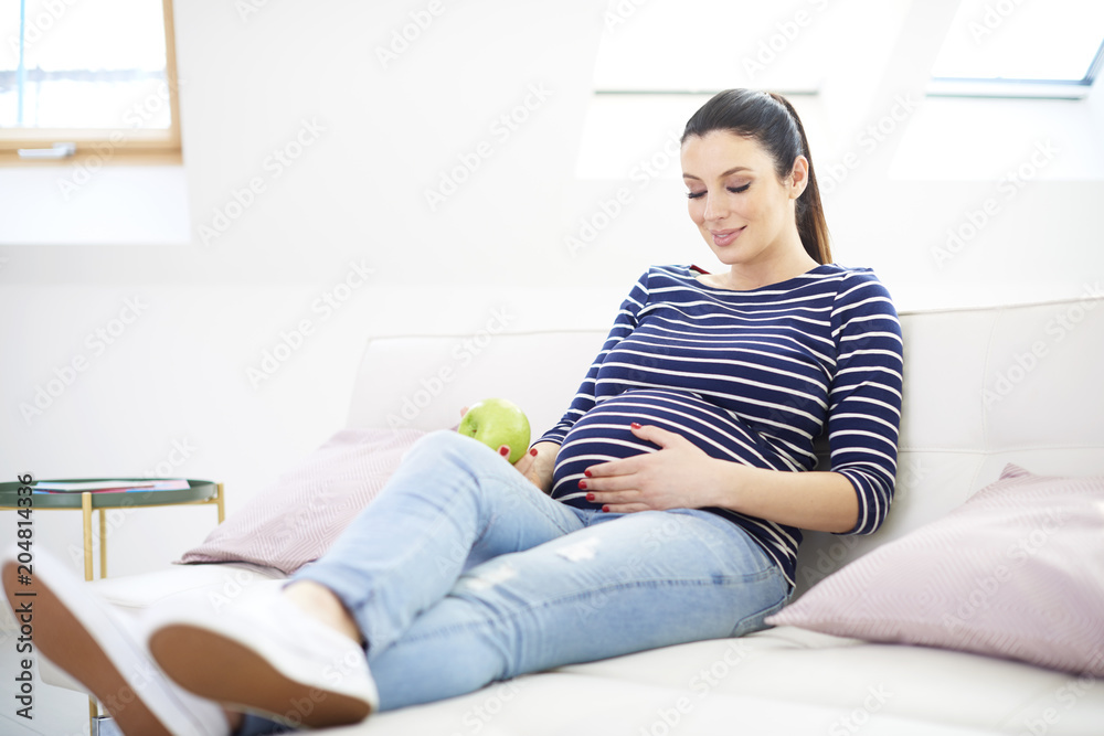 Portrait of beautiful pregnant woman with hands on her baby bump ejoying her pregnancy while relaxing on sofa at home. Portrait of beautiful pregnant woman with hands on her baby bump ejoying her pregnancy while relaxing on sofa at home.