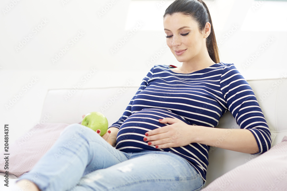 Portrait of beautiful pregnant woman with hands on her baby bump ejoying her pregnancy while relaxing on sofa at home. Portrait of beautiful pregnant woman with hands on her baby bump ejoying her pregnancy while relaxing on sofa at home.