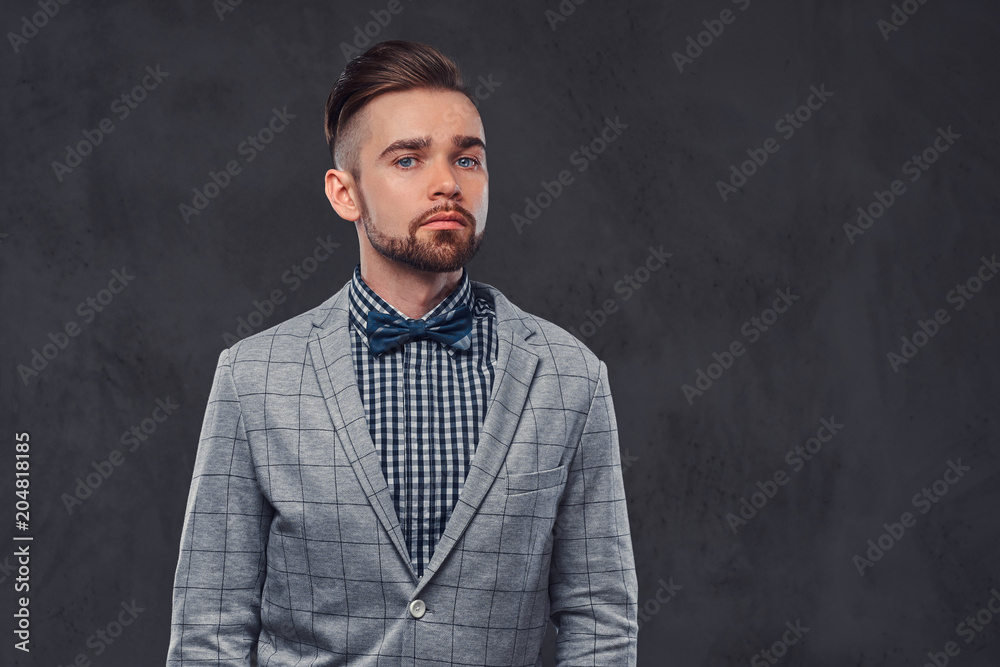 Confident stylish bearded man with hairstyle in an elegant retro gray suit and bow tie, posing in a studio.