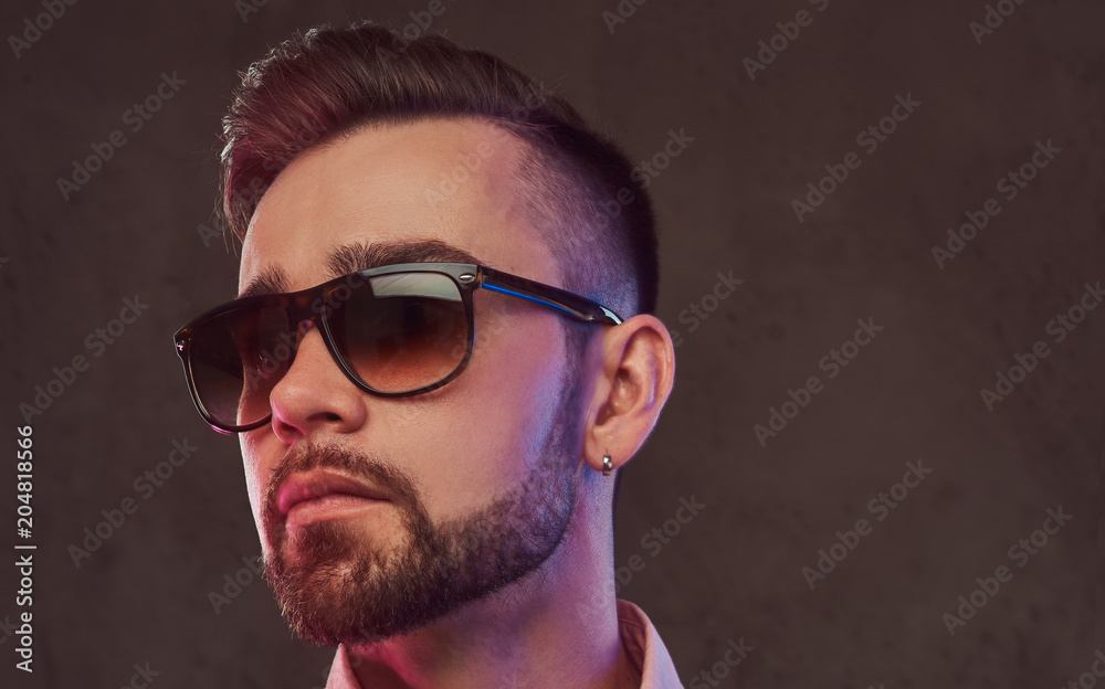 Close-up portrait of a confident stylish bearded man with hairstyle and sunglasses in a gray suit and pink shirt, posing in a studio. Close-up portrait of a confident stylish bearded man with hairstyle and sunglasses in a gray suit and pink shirt, posing in a studio.