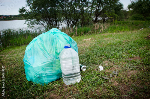 full green garbage bag and open plastic water bottle on the grass in nature by river