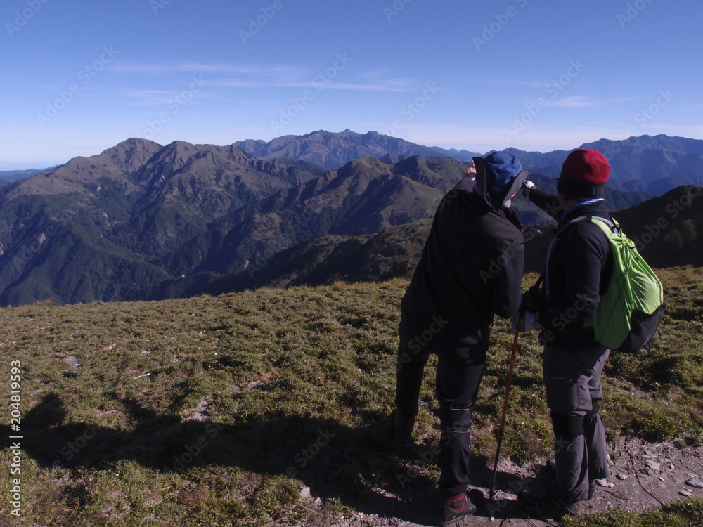 Two male hikers are pointing at the mountains far away and talking about what the names of those mountain are. Two male hikers are pointing at the mountains far away and talking about what the names of those mountain are.