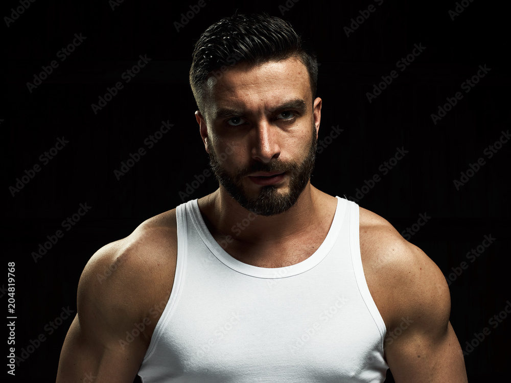 A strong, a serious, muscular man in a white t-shirt is worth and looks in camera. He's got the beard on the face and different emotions A strong, a serious, muscular man in a white t-shirt is worth and looks in camera. He's got the beard on the face and different emotions