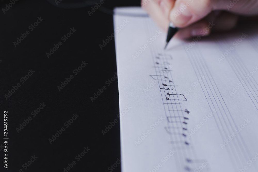 Fototapeta premium Side view of the hand writing the music notes with pencil. The concept of the music creating, composing, note writing, music art.