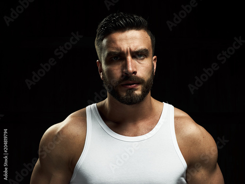 A strong, a serious, muscular man in a white t-shirt is worth and looks in camera. He's got the beard on the face and different emotions