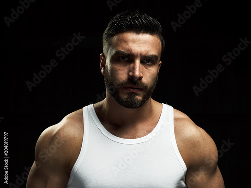 A strong, a serious, muscular man in a white t-shirt is worth and looks in camera. He's got the beard on the face and different emotions