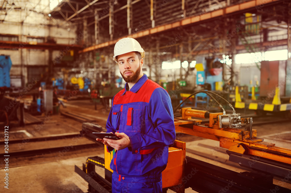 Man working in a construction helmet with a tablet on the background of a plant Man working in a construction helmet with a tablet on the background of a plant