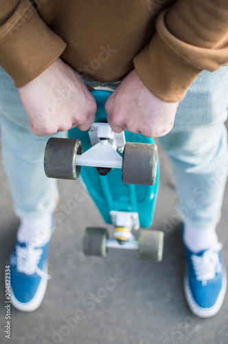 Perspective view of the youn hipster holding blue plastic penny skateboard. The concept of city travelling, vlogging, modern lifestyle