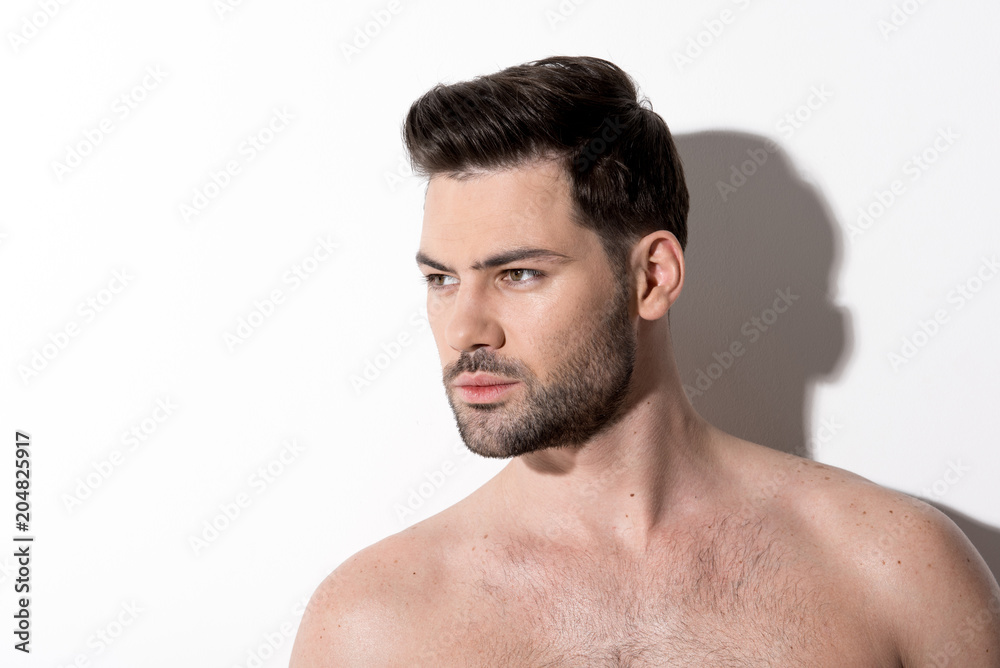 Side view of gorgeous young bearded naked man is standing and looking aside thoughtfully. Copy space in the left side. Beauty concept Side view of gorgeous young bearded naked man is standing and looking aside thoughtfully. Copy space in the left side. Beauty concept
