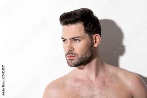 Side view of gorgeous young bearded naked man is standing and looking aside thoughtfully. Copy space in the left side. Beauty concept