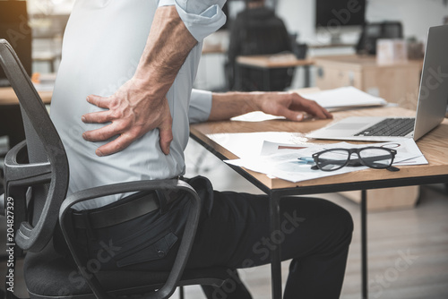 Employer having pain in back. He holding it by hand while sitting at table during job. Worker with bad state of health concept