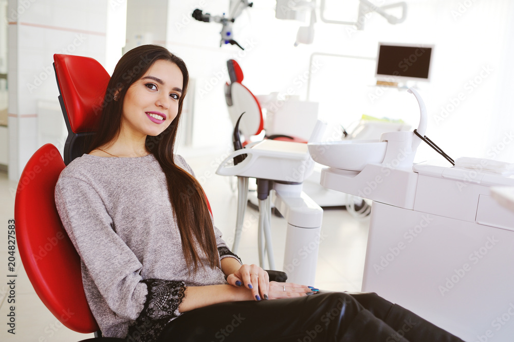 Portrait of a beautiful girl in a red dental chair on the background of a modern clinic Portrait of a beautiful girl in a red dental chair on the background of a modern clinic