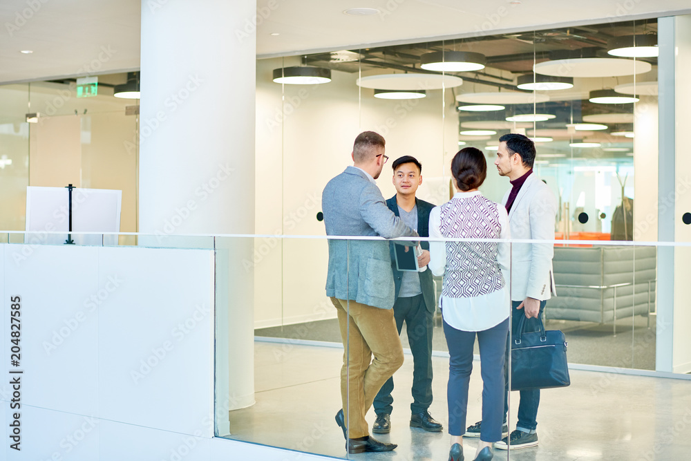 Full length portrait of group of young business people standing in circle in modern office building discussing project, copy space