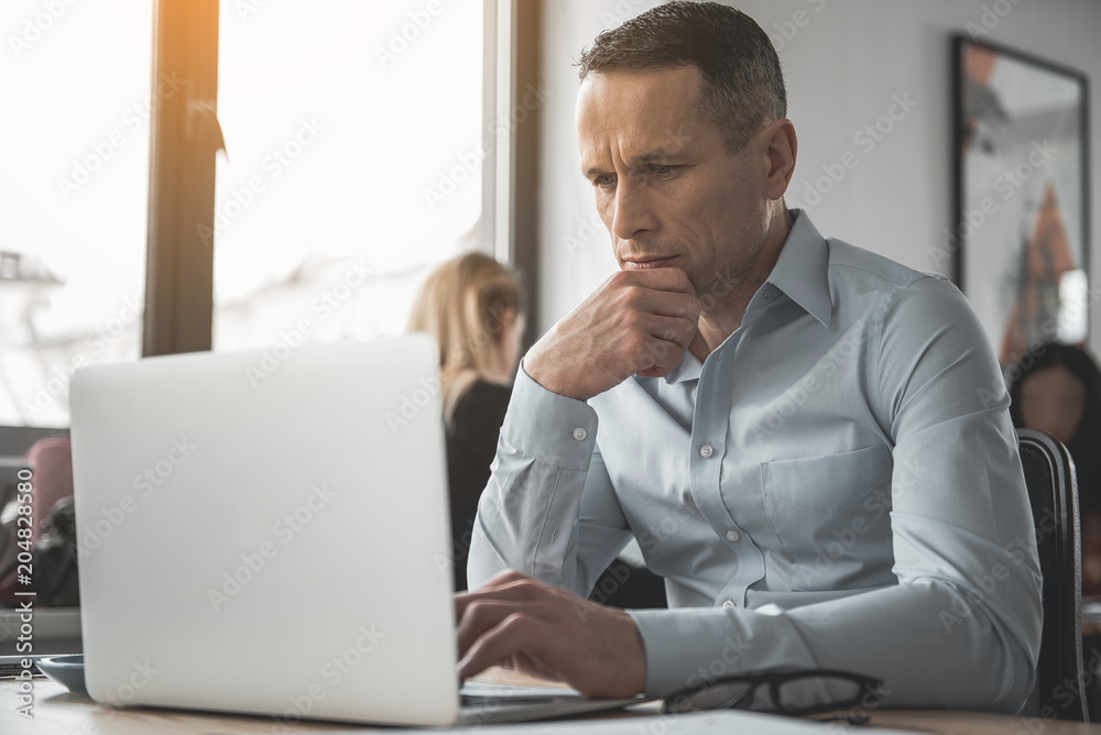 Portrait of focused businessman looking at notebook computer while sitting at table. Undistracted employer concept Portrait of focused businessman looking at notebook computer while sitting at table. Undistracted employer concept