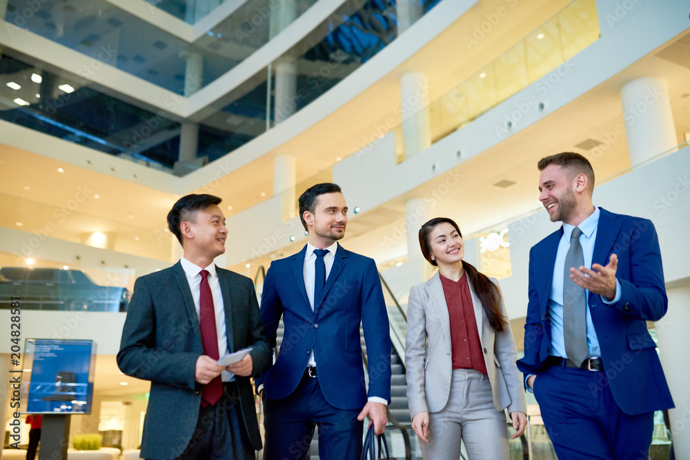 Group of cheerful young business people smiling happily while chatting on their way leaving modern office building Group of cheerful young business people smiling happily while chatting on their way leaving modern office building