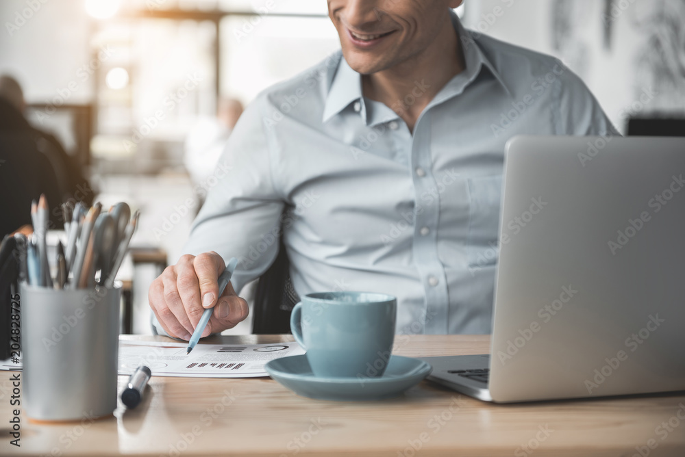 Outgoing male working with document while using gadget. He situating at table. Glad businessman at job concept Outgoing male working with document while using gadget. He situating at table. Glad businessman at job concept