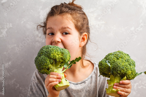 Little beautiful girl eating broccoli. Healthy vegan baby foods.