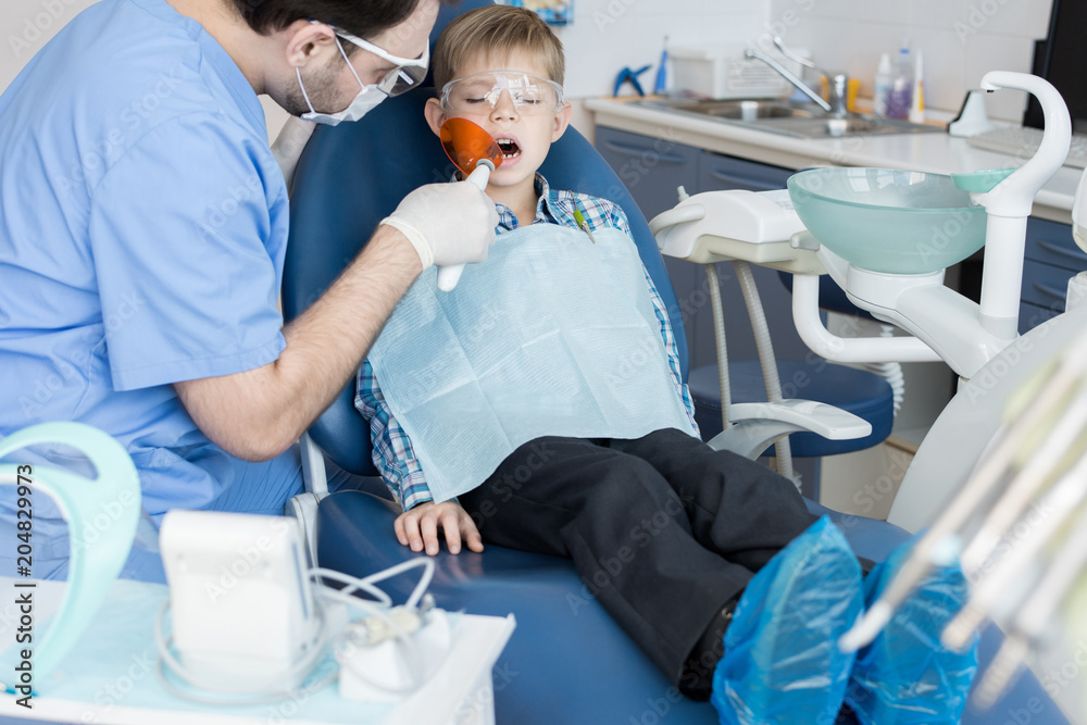 Portrait of cute little boy sitting in dental chair during laser teeth treatment in modern clinic, copy space