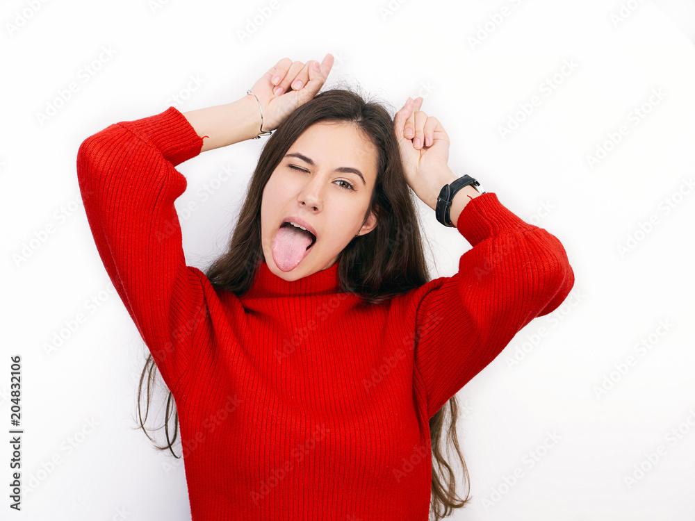 Young beautiful brunette woman in red sweater showing horns with her fingers posing against white background Young beautiful brunette woman in red sweater showing horns with her fingers posing against white background