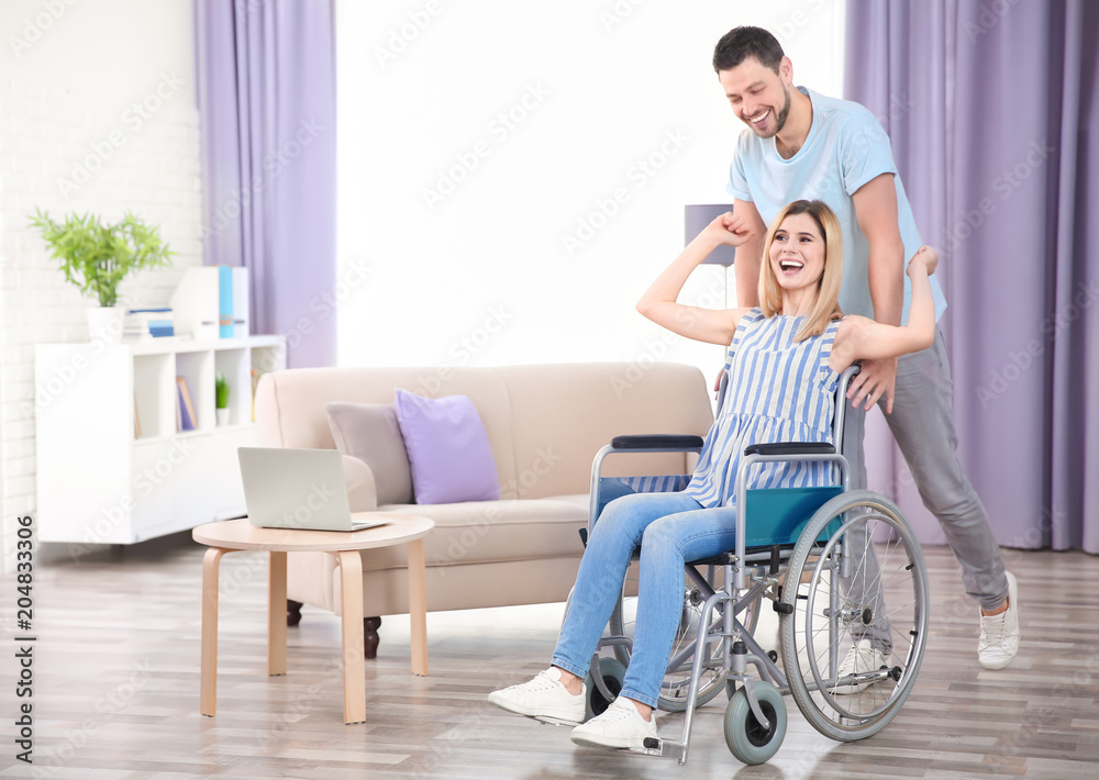 Young man taking care of woman in wheelchair indoors